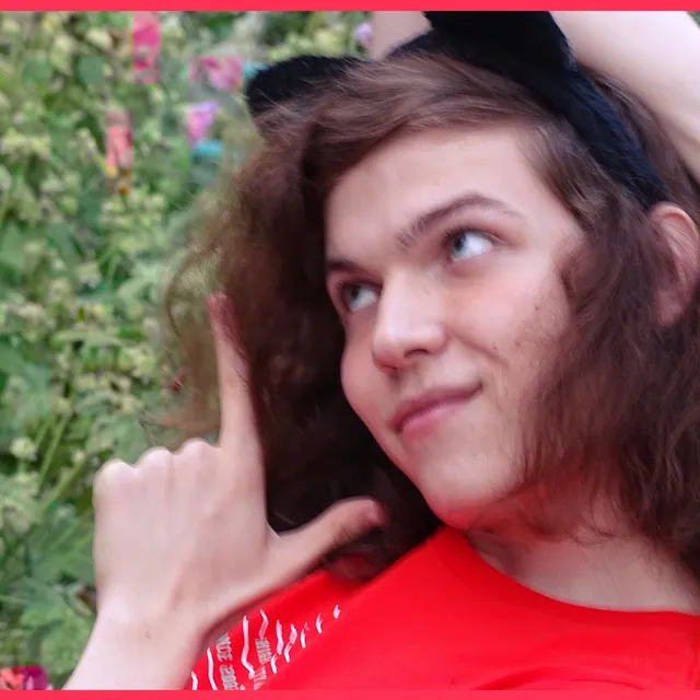 Teenage Liz with long brown hair and a cat-ear headband, pointing up, in a red T-shirt